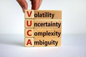 Volatility Uncertainty Complexity Ambiguity stacking wooden blocks with adult fingers stacking them.